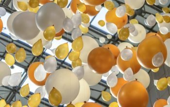 Vibrant arrangement of orange, white, and yellow balloons hanging in an indoor celebration space.